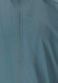 Ljusblå idrottsjacka med full dragkedja framtill, gjord av mjukt och lätt tyg. Har en diskret logotyp och platta sömmar.