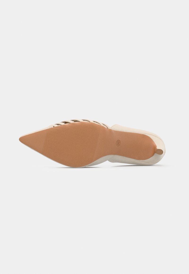 Zapato de tacón alto beige con punta afilada, que presenta una suela de goma texturizada y detalles recortados a lo largo del diseño superior.