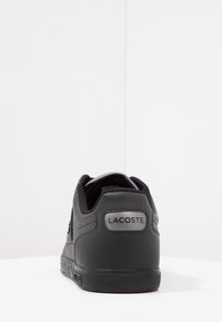 Svart Lacoste-sneaker med en texturerad läderoversida, släta detaljer, vadderad krage och varumärkesmärkning på hälkappan. Enkel snördesign.