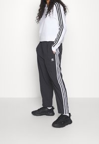 White long-sleeve top with black stripes on sleeves, paired with black track pants featuring white stripes, and black athletic shoes.
