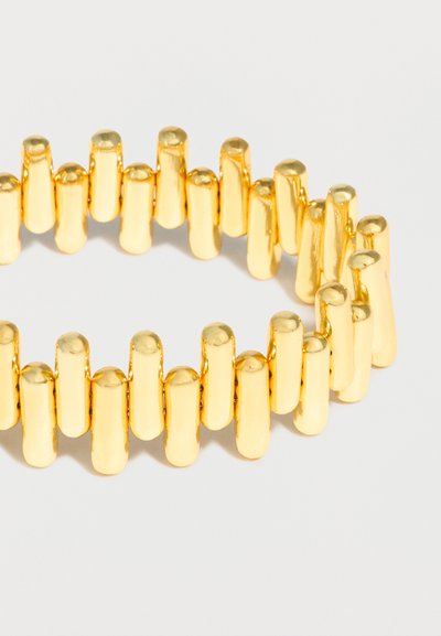 Χρυσό βραχιόλι με κάθετες, μπαρ-σχήματος συνδέσεις τοποθετημένες σε εναλλασσόμενο μοτίβο σε ουδέτερο φόντο.