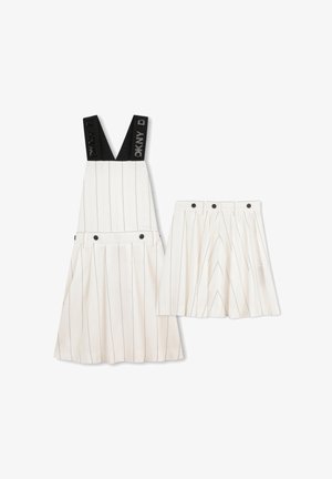 Jupe blanche à fines rayures et robe salopette assortie avec des détails de boutons noirs et des bretelles noires marquées DKNY sur la salopette.