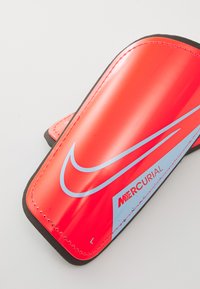 Red Nike Mercurial shin guard with a smooth surface, blue accents, black border, and adjustable strap for secure fit.