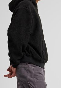 Haut à capuche en polaire noir avec une finition texturée, doté d'une poche kangourou et d'un ourlet côtelé. Assorti à un pantalon en corduroy gris clair.