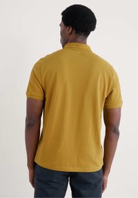 Sennepsgul polo skjorte med korte ærmer, en traditionel krave og lige kanten. Tekstureret stof med minimale sømme.