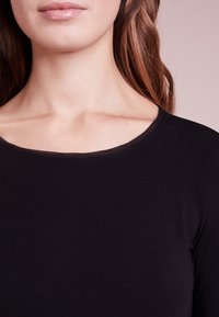 Schwarzes Langarmoberteil mit einem breiten, abgerundeten Ausschnitt und einer glatten Textur, das eine figurbetonte Silhouette ohne sichtbare Nähte zeigt.