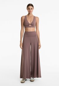 Texturerad, mauve croptop med knutdetalj och nyckelhålsutsnitt, kombinerat med högmidjade, vida byxor i matchande färg och mjukt material.