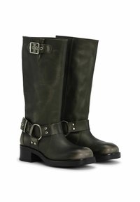 Magas, olíva zöld bőr csizmák kerek orral, csattal és pántos díszítésekkel, valamint tömbsarokkal. Simább textúrával rendelkezik.