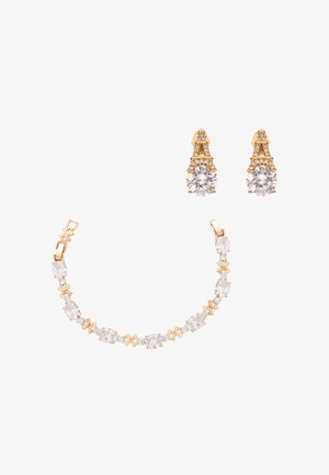 Brățară aurie cu pietre clare ovale și zale delicate aurii, asortată cu cercei cu știft aurii în forma Turnului Eiffel, cu pietre clare rotunde.