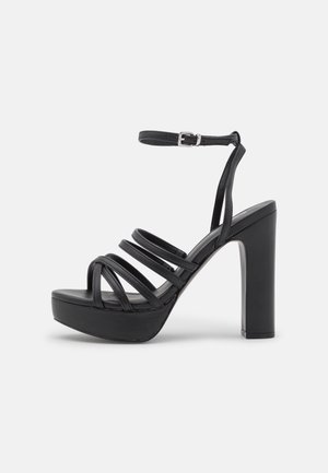 Zwarte hoge hakken sandalen met een platform. Heeft meerdere dunne banden over de voet en een enkelband met een metalen gesp.