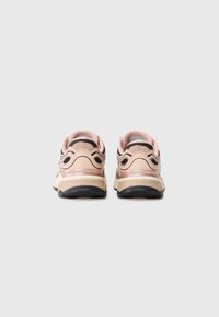 Een paar beige en roestige roze sport sneakers weergegeven vanaf de achterkant tegen een effen lichtgrijze achtergrond.