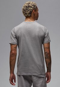 T-shirt in cotone grigio con collo rotondo, maniche corte e vestibilità rilassata. La vista posteriore mostra una texture liscia e dettagli di cucitura sottili.