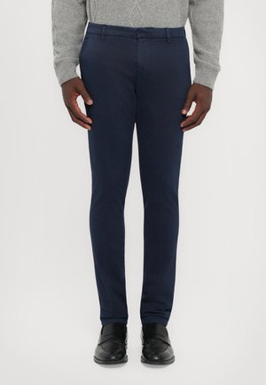 Pantaloni tailored blu navy, slim fit con materiale in cotone liscio. Presentano una parte frontale piatta, passanti per la cintura e tasche laterali. Abbinati a scarpe nere.