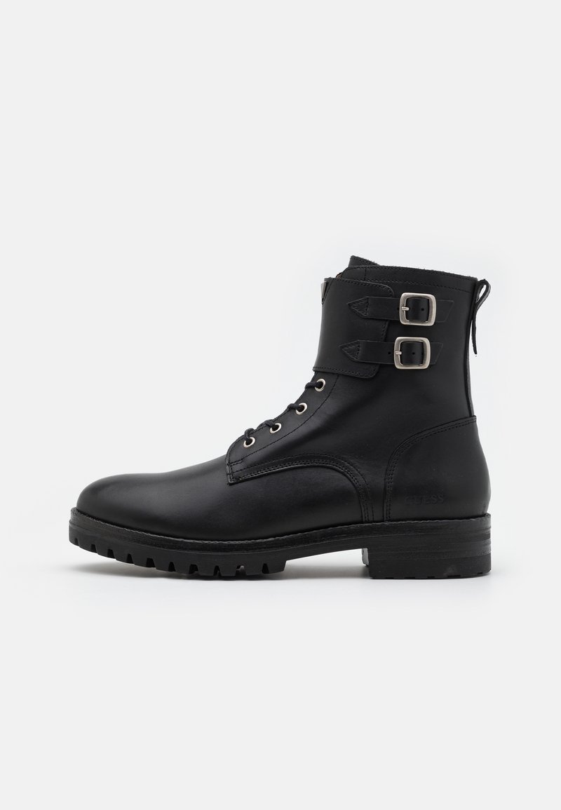 Bottine en cuir noir avec bout arrondi, laçage à l'avant, deux boucles en métal et semelle en caoutchouc texturée. Finition lisse, design robuste.