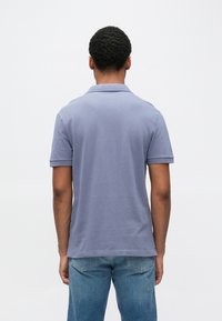 Polokošeľa s krátkym rukávom v svetlomodrej látke, s klasickým golierom a úzkym strihom, v kombinácii so svetlomodrými džínsami.