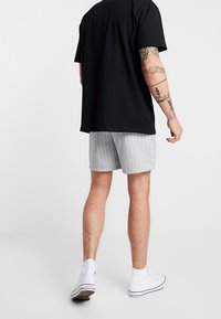 Černé bavlněné tričko, šedé pruhované šortky, bílé tenisky. Zaměření na zadní pohled, který ukazuje textury látek a designové prvky.