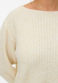 Cream-colored knitted sweater with a loose fit, featuring a wide neckline and a textured pattern of small holes throughout.