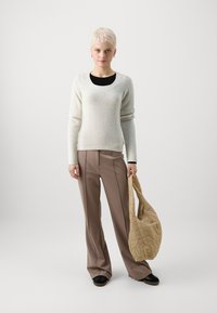 Gaišs krēms džemperis, brīvs piegriezums, ribotas piedurknes; brūnas platās bikses ar šuvju detaļām; kvaltēts beisgs somiņš. Melnas kurpes. Vienkārša fons.