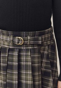 Black ribbed sweater paired with a green plaid skirt, featuring a gold buckle belt and vertical pleats, showcasing a textured fabric.