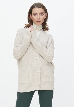 Beige gestrickte Strickjacke mit gerippter Textur, oversized Schnitt und zwei Fronttaschen; verfügt über einen V-Ausschnitt und Holzknöpfe.