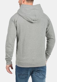 Grijze sweatshirt met capuchon, gemaakt van zacht materiaal. Heeft een eenvoudig ontwerp en ribbelmanchetten. G gedragen met een blauwe spijkerbroek.