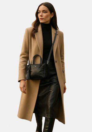 Sac en cuir noir avec une finition texturée, poignées courtes et bandoulière amovible, porté avec un manteau beige et une jupe noire.