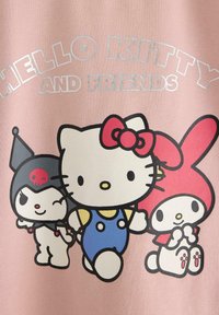 Tessuto rosa con "Hello Kitty and Friends" che presenta i personaggi: Hello Kitty in salopette blu, un fiocco rosso e amici in abiti distintivi.