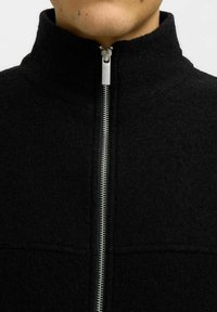 Svart fleecejacka med hög krage, utrustad med en silvermetalldragkedja fram och en texturerad yta.