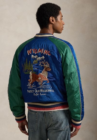 Chaqueta bomber azul y verde con una escena de vida silvestre bordada, las palabras "Wyoming" y "Protejamos nuestra naturaleza" en la parte trasera, y puños a rayas.