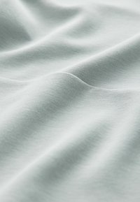 Țesătură de bumbac verde deschis cu o textură netedă, evidențiind pliuri moi și umbrire subtilă pe întreaga suprafață a materialului.