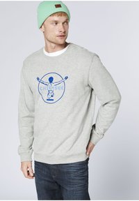 Gray sweatshirt featuring blue graphic design with a person in a circular outline. Ribbed cuffs and hem, paired with dark jeans.