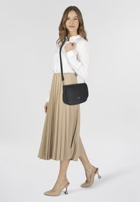 Borsa a tracolla nera con una texture in pelle liscia, accessori in argento e una forma rettangolare sottile, abbinata a una blusa bianca e una gonna plissettata beige.