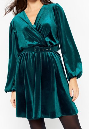 Teal fluwelen jurk met een wikkelontwerp, lange pofmouwen, een ceintuur met gespdetails en een uitlopende rok.