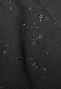 Svart tyg med en slät yta som har flera vattendroppar, vilket indikerar vattentålighet. Ytan verkar något blank.