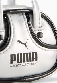 Borsa a tracolla in finta pelle argento con dettagli neri, forma piccola e rotonda, duali manici e logo Puma in evidenza con lettere nere.