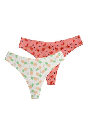 Frau trägt weiße Bikinihose mit orangefarbenem Ananasdruck und ein weißes, geknotetes Hemd mit hochgekrempelten Ärmeln.