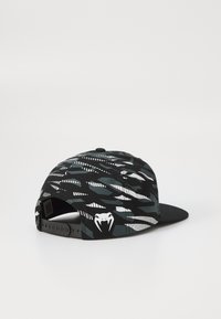 Melna snapback cepure ar abstraktu rakstu pelēkā un baltā krāsā, ar baltu čūskas logo aizmugurē un plakanu viziera dizainu.