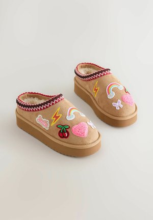 Beige Slip-On-Clogs mit strukturierter Oberfläche, flauschigem Futter und bunten, gestickten Aufnähern von Regenbögen, Kirschen und Herzen; Gummisohle.