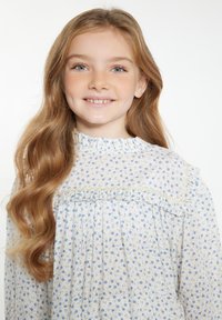 Hvid bluse med blåt blomster mønster, flæsekrave og blondekant. Blødt, let stof, lange ærmer. Smilende barn med bølget hår.