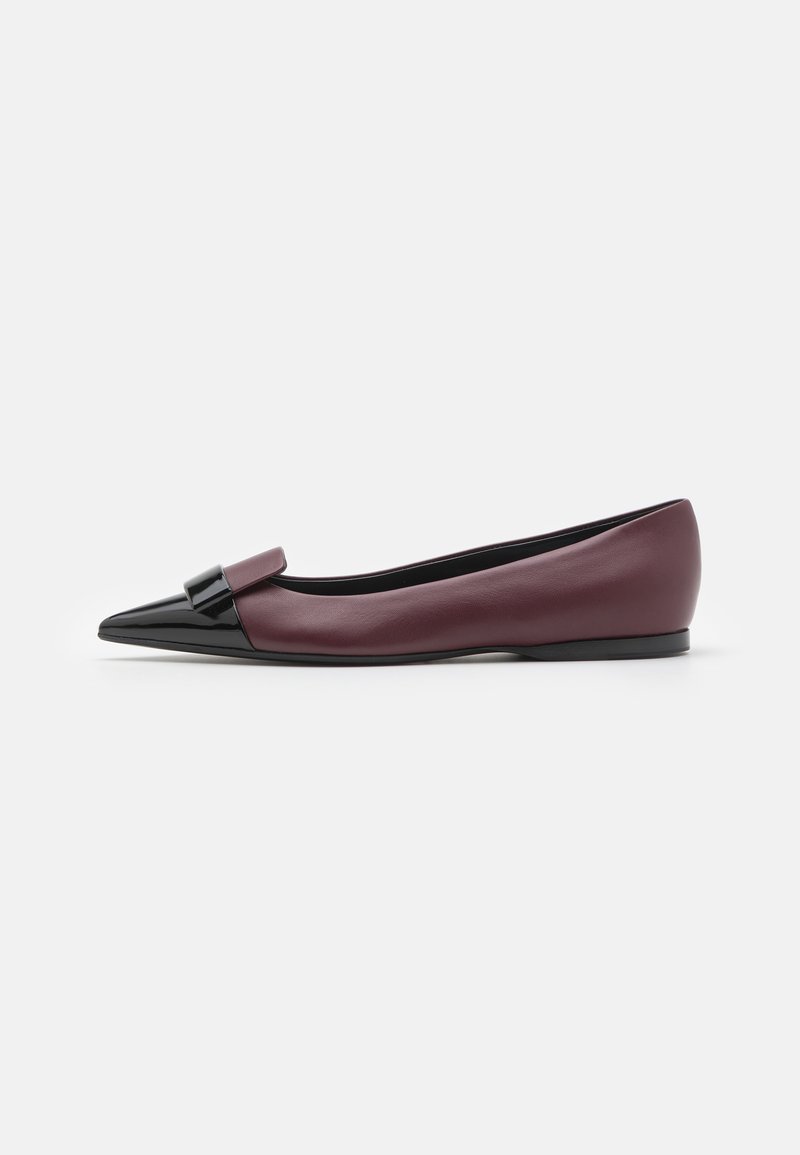 Zapato plano de cuero burdeos con punta afilada, detalle brillante negro y moño decorativo en la parte superior. Textura suave, diseño minimalista.