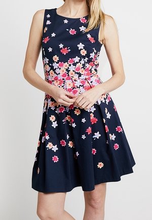 Marineblauwe bloemenjurk met mouwloos ontwerp, getailleerde taille en uitlopende rok, versierd met roze, paarse en gele bloemmotieven.