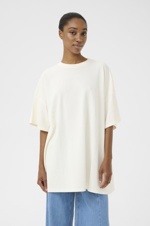 Übergrößiges T-Shirt in Creme aus weichem Baumwollstoff, mit Rundhalsausschnitt und kurzen Ärmeln. Kombiniert mit hellblauen weiten Jeans.