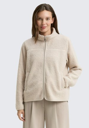 Beige fleece jacket met een rits aan de voorkant, hoge kraag en twee zijzakken. Beschikt over een gladde naaddetail over de borst.