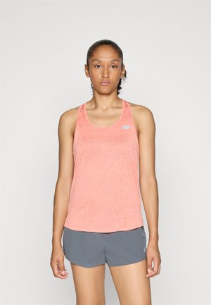 Femme se tenant de face, portant un débardeur de sport corail sans manches et un short de course gris, devant un fond uni.
