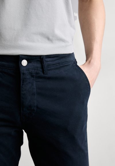 Granatowe bawełniane spodnie o gładkiej fakturze, z zapięciem na guzik z przodu, bocznymi kieszeniami i slim fit.