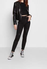 Cazadora de cuero negra de estilo biker combinada con un top negro recortado y jeans rasgados negros. La modelo lleva zapatillas altas negras.