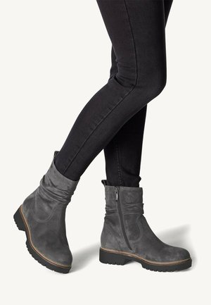 Grau Wildleder-Ankle Boots mit einem lässigen Design, seitlichem Reißverschluss, strukturiertem Obermaterial und kontrastierender Naht, kombiniert mit schwarzen, eng anliegenden Jeans.