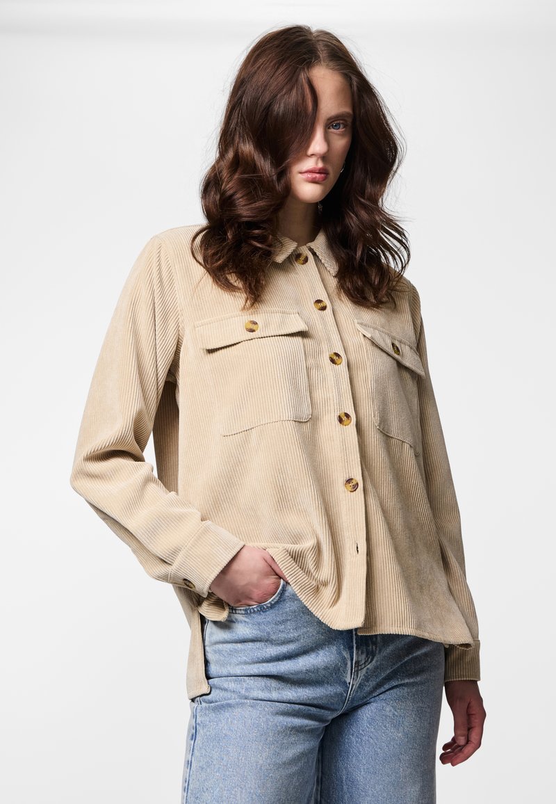 Beige corduroy-paita, jossa napillinen etuosa, kaksi rintataskua ja pitkät hihat. Paita on väljää mallia ja siinä on teksturoitu kangas.