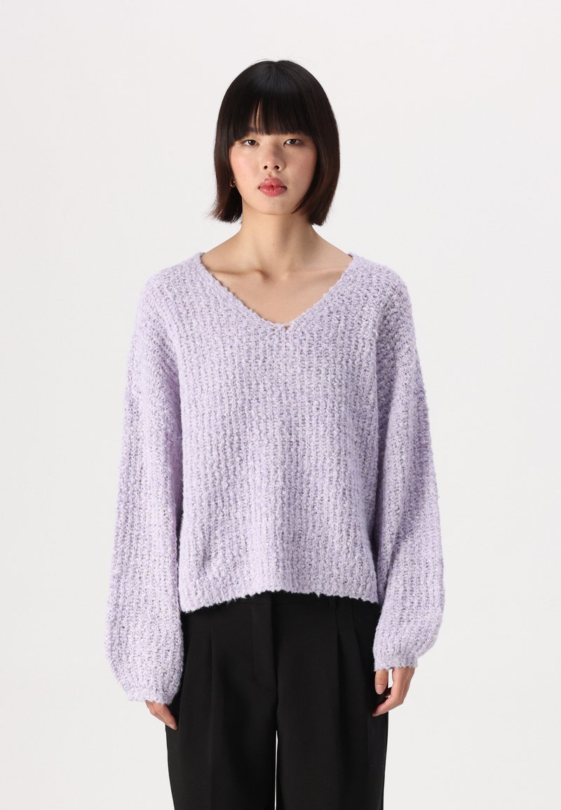 Sweater de linho lavanda claro com um padrão de malha texturada, corte solto e mangas bufantes; combinado com calças largas pretas.