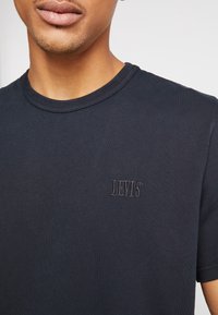Granatowa bawełniana koszulka z okrągłym dekoltem, z haftowanym logiem "LEVI'S" na lewej piersi. Tkanina ma gładką teksturę.
